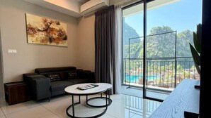 Un salon moderne avec un canapé, une table basse ronde et une grande fenêtre donnant sur une montagne et une piscine.