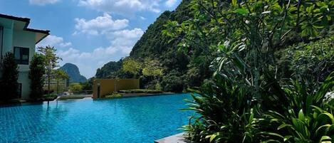 A swimming pool with clear blue water, surrounded by lush greenery and a mountain backdrop.
