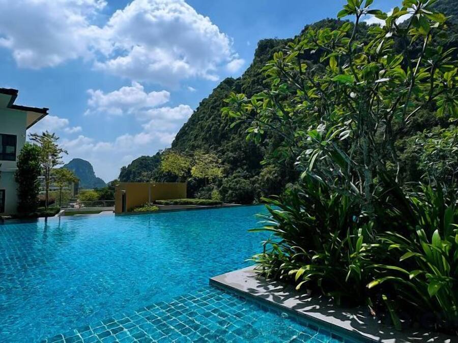 A swimming pool with clear blue water, surrounded by lush greenery and a mountain backdrop.
