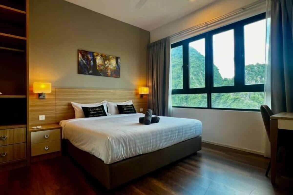 Une chambre d’hôtel avec un grand lit, deux lampes de chevet, un tableau au mur et une vue sur la verdure par la fenêtre.