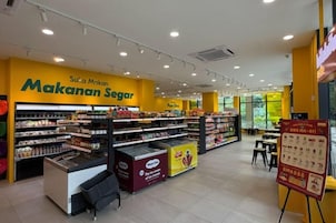 A grocery store interior with shelves stocked with products, a yellow sign reading 'Makanan Segar,' and a promotional stand.