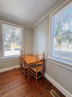 A room with a wooden table and chairs, large windows with blinds, and hardwood flooring.
