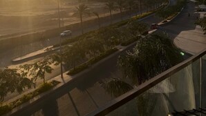 Vista al atardecer desde un balcón con vista a una calle bordeada de palmeras y farolas.