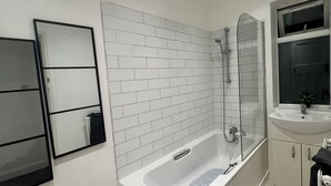 Ein modernes Badezimmer mit einer weißen Duschkabine, einer großzügigen Badewanne, einer Dusche mit Glastrennwand, einem weißen Waschbecken und einem Spiegel.