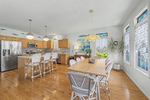 A kitchen with wooden cabinets, stainless steel appliances, a dining area with wicker chairs, and a large window with a view. - Gorgeous 5BR 3BA Home, close to beach, Town + playground; full linen service (Ocean City)