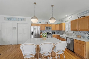 A kitchen with wooden cabinets, a stainless steel refrigerator, a microwave, and a central island with chairs. - Gorgeous 5BR 3BA Home, close to beach, Town + playground; full linen service (Ocean City)