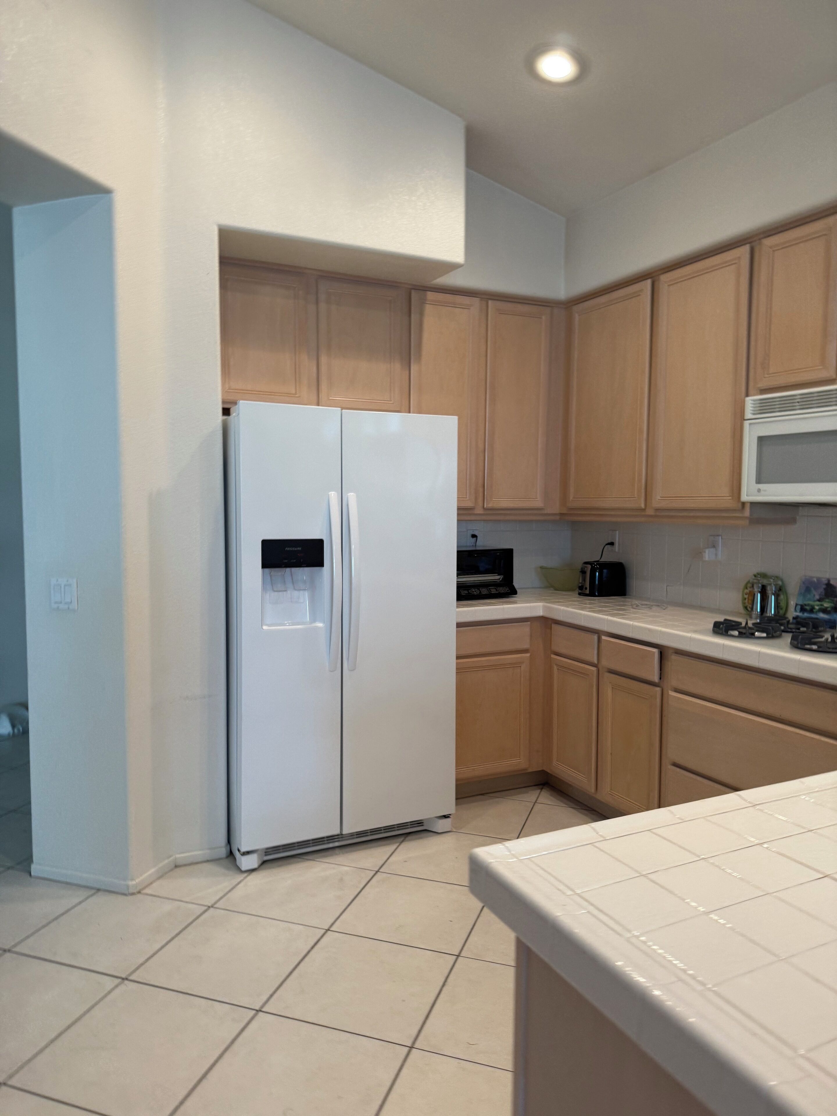 A kitchen with a white refrigerator, wooden cabinets, a microwave, and a tiled floor.
