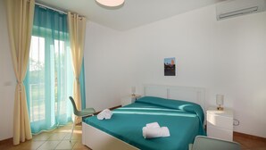 Hotellihuone, jossa on sänky, tuoli, yöpöytä, taulu seinällä ja ikkuna, jossa on verhot.