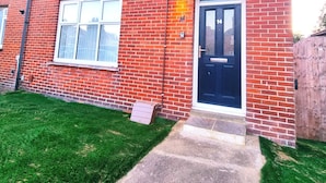 A red brick two-story residential building with a black front door, white-framed windows, and a small front garden. - Forge Lane Cozy Apartment (Gillingham)