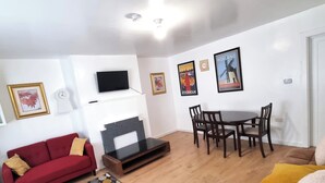 A living room with a red sofa, a brown sofa, a TV mounted on the wall, a fireplace, a dining table with chairs, and two framed pictures on the wall. - Forge Lane Cozy Apartment (Gillingham)