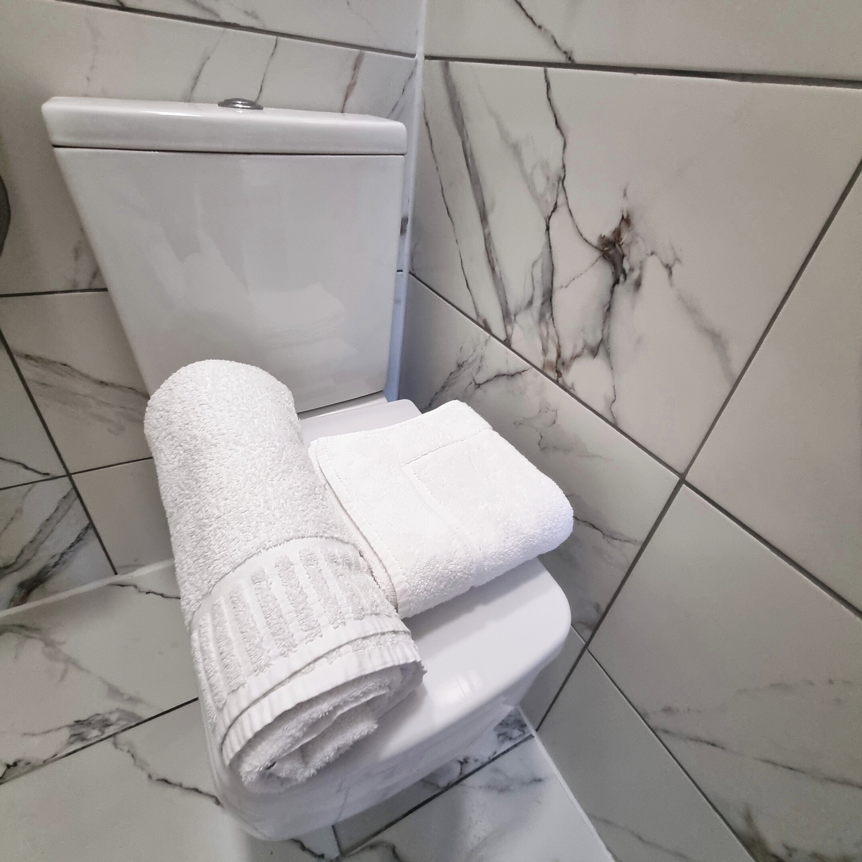 Un bagno con il water, asciugamani bianchi e piastrelle in marmo.