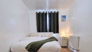 A bedroom with a bed, a nightstand, a lamp, and a radiator. - Forge Lane Cozy Apartment (Gillingham)