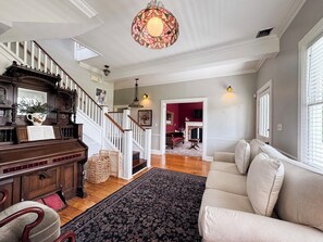 A spacious living room with a fireplace, a staircase with wooden railings, and a large chandelier. - Historic Beaufort Estate - Near Downtown Beaufort & Parris Island (Beaufort)