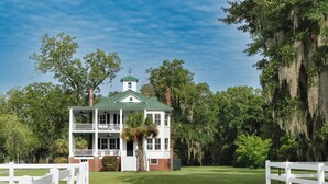 A two-story white building with a green roof, surrounded by lush greenery and a white fence. - Historic Beaufort Estate - Near Downtown Beaufort & Parris Island (Beaufort)