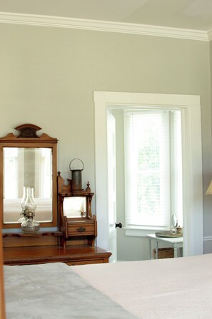Une chambre à coucher avec un lit, une commode, un miroir et une fenêtre avec des stores.