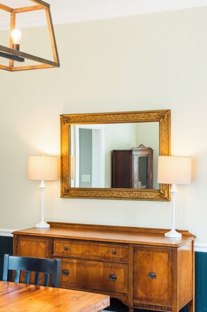 A dining area with a wooden table, two chairs, a cabinet, and a large ornate mirror with a gold frame. - Historic Beaufort Estate - Near Downtown Beaufort & Parris Island (Beaufort)