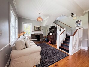 A spacious living room with a sofa, a fireplace, a staircase, and a chandelier. - Historic Beaufort Estate - Near Downtown Beaufort & Parris Island (Beaufort)
