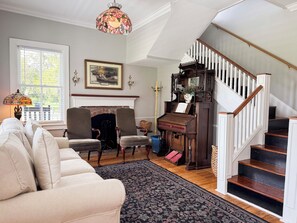 A living room with a fireplace, a piano, a staircase, and a large window. - Historic Beaufort Estate - Near Downtown Beaufort & Parris Island (Beaufort)