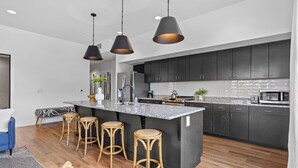 A modern kitchen with dark cabinets, a granite island with bar stools, and pendant lighting. - 2 Condos-8 Minutes to Broadway-Walkable-5 King (Nashville)