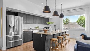 A modern kitchen with a large island, stainless steel appliances, and wooden stools. - 2 Condos-8 Minutes to Broadway-Walkable-5 King (Nashville)