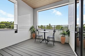 A balcony with a table and chairs, potted plants, and a view of greenery.