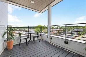 A balcony with a table and chairs, a potted plant, and a view of the cityscape.