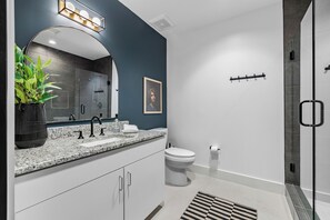 A modern bathroom with a granite countertop, white fixtures, a large mirror, and a shower area.