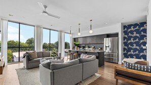 A modern living room with a grey sectional sofa, a wooden bench, and a large window offering a view of the outdoors. - 2 Condos-8 Minutes to Broadway-Walkable-5 King (Nashville)