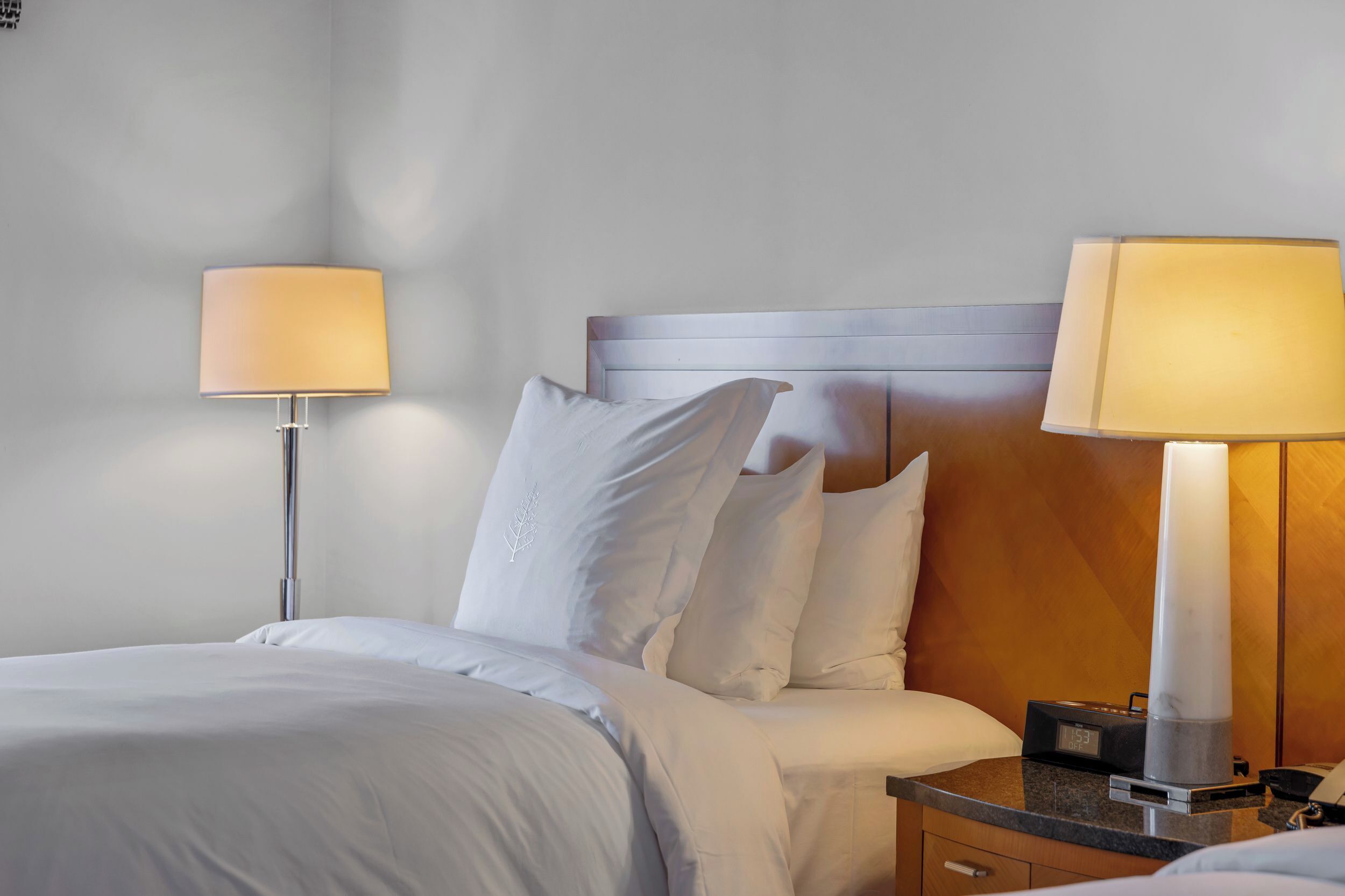 Une chambre d’hôtel avec un lit bien fait, deux lampes de chevet, une table de chevet avec une horloge et une tête de lit en bois.