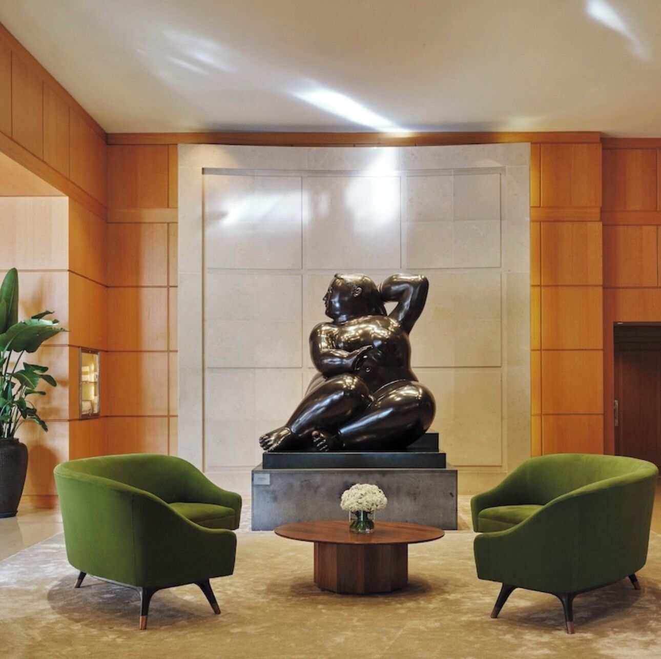 Un hall d’entrée agrémenté d’une sculpture moderne, de deux fauteuils verts et d’une petite table sur laquelle est posé un vase.