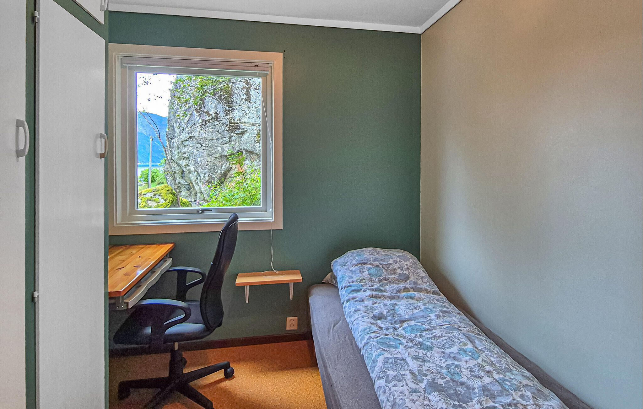 Una habitación pequeña con una cama individual, un escritorio con silla y ventana con vista a zonas verdes.