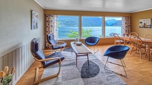 Ein Zimmer mit Blick auf einen See und Berge, möbliert mit Stühlen und einem Tisch.