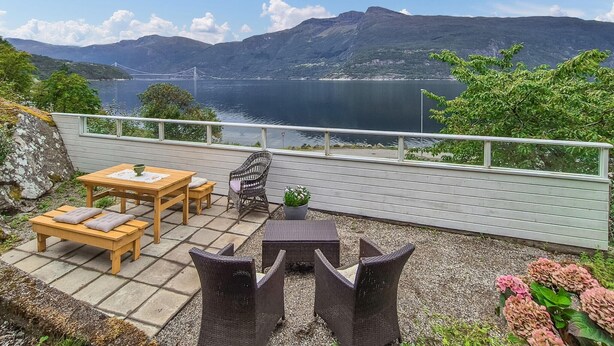 Eine Terrasse mit Holztisch und Stühlen, ein Korbstuhl und ein Blumentopf.