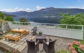 Une terrasse avec une table et des chaises en bois, un fauteuil en osier et une plante en pot.