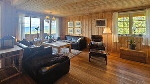 A cozy living room with wooden walls and floors, a black leather sofa, a wooden coffee table, and a fireplace. There are framed pictures on the wall and a telescope on a tripod near the window. - Awesome home in Eggedal with sauna (Eggedal)