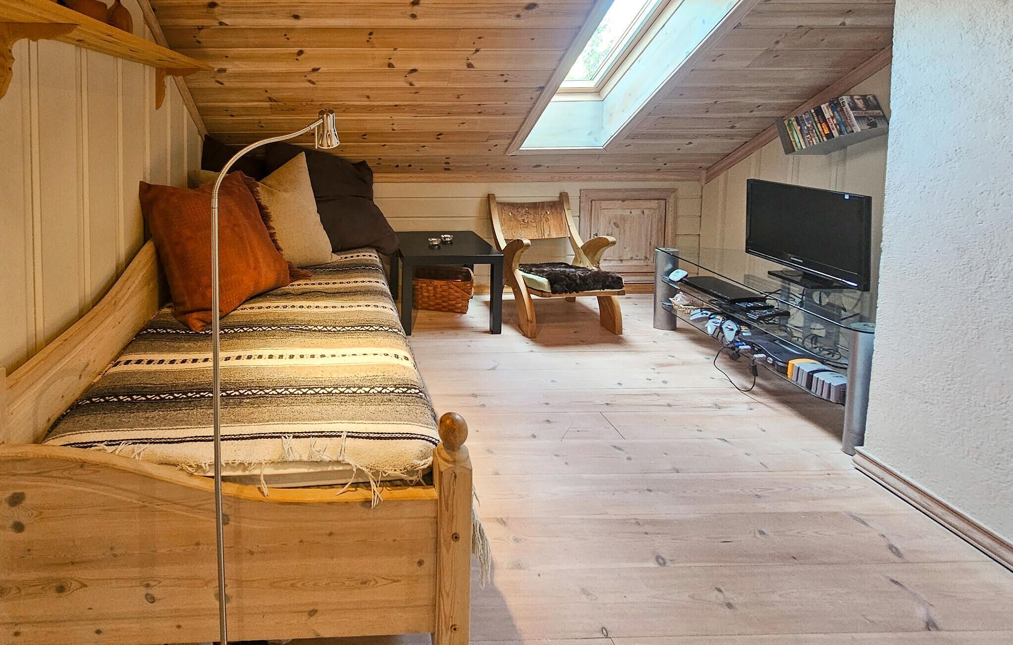 Ein gemütliches Zimmer mit Holzbalkendecke, einer Couch, einem Sessel, einem kleinen Tisch und einem Fernseher.