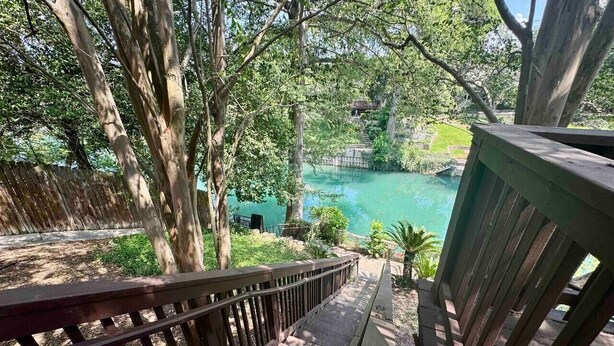A wooden deck with a railing overlooking a turquoise pool surrounded by trees.