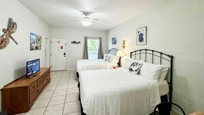 A hotel room with two beds, a wooden dresser, a television, and a ceiling fan.