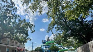 A parking lot with a water park in the background, including a green water slide and a building with a sign that reads "D's Homemade Pizza".