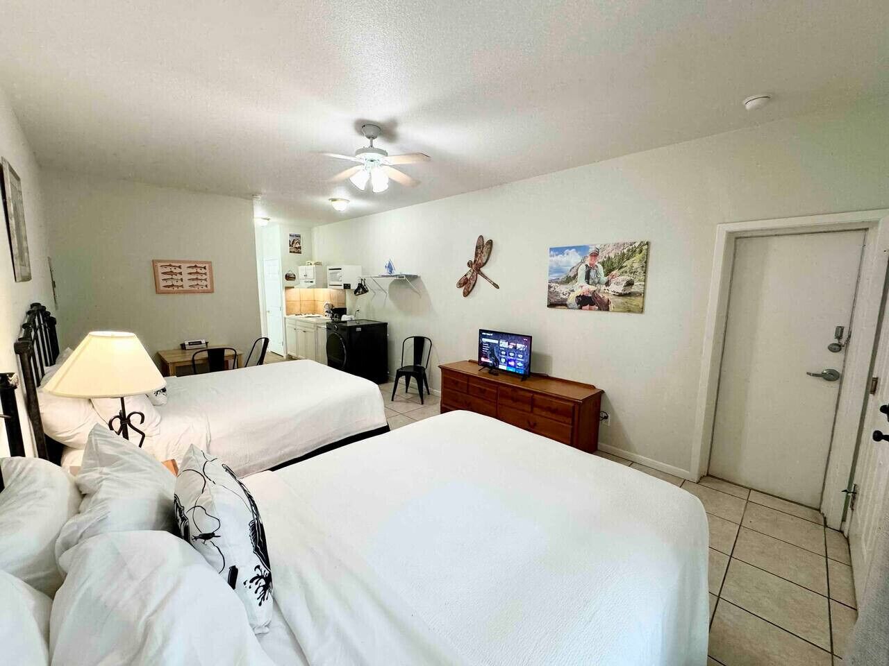 A hotel room with two beds, a desk with a computer, a chair, a television, and a door.