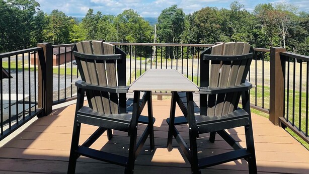 A deck with a table and chairs, overlooking a parking area and greenery.