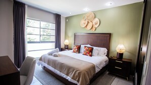 A hotel room with a large bed, two bedside tables with lamps, a chair, and a view of the outdoors through a window.