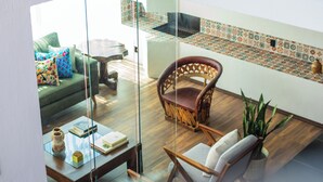 A modern living room with a glass partition, a green sofa, a wooden coffee table, and a wicker chair.
