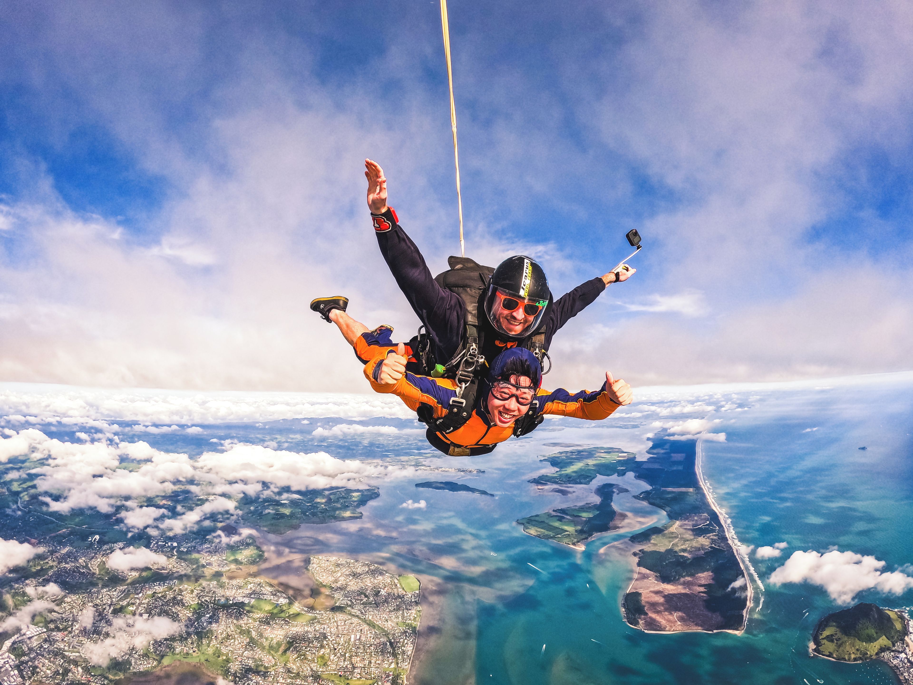 A person skydiving with a parachute above a coastal landscape.