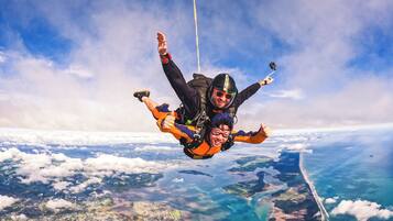 A person skydiving with a parachute above a coastal landscape.