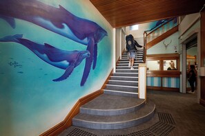 A staircase with a mural of whales, a wooden ceiling, and a reception area with a counter and a mirror. - Wanderlust NZ (Tauranga)
