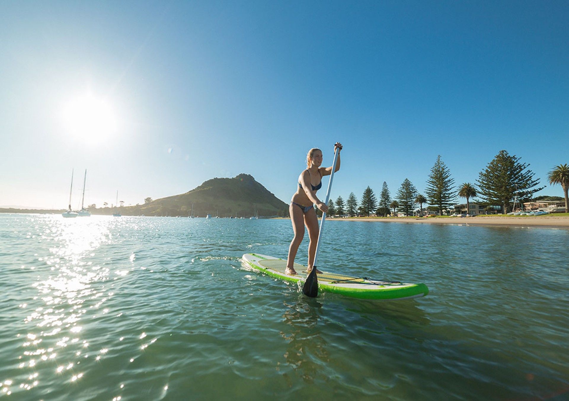 Una persona haciendo paddleboard sobre aguas tranquilas, con cielo despejado y un paisaje montañoso al fondo.