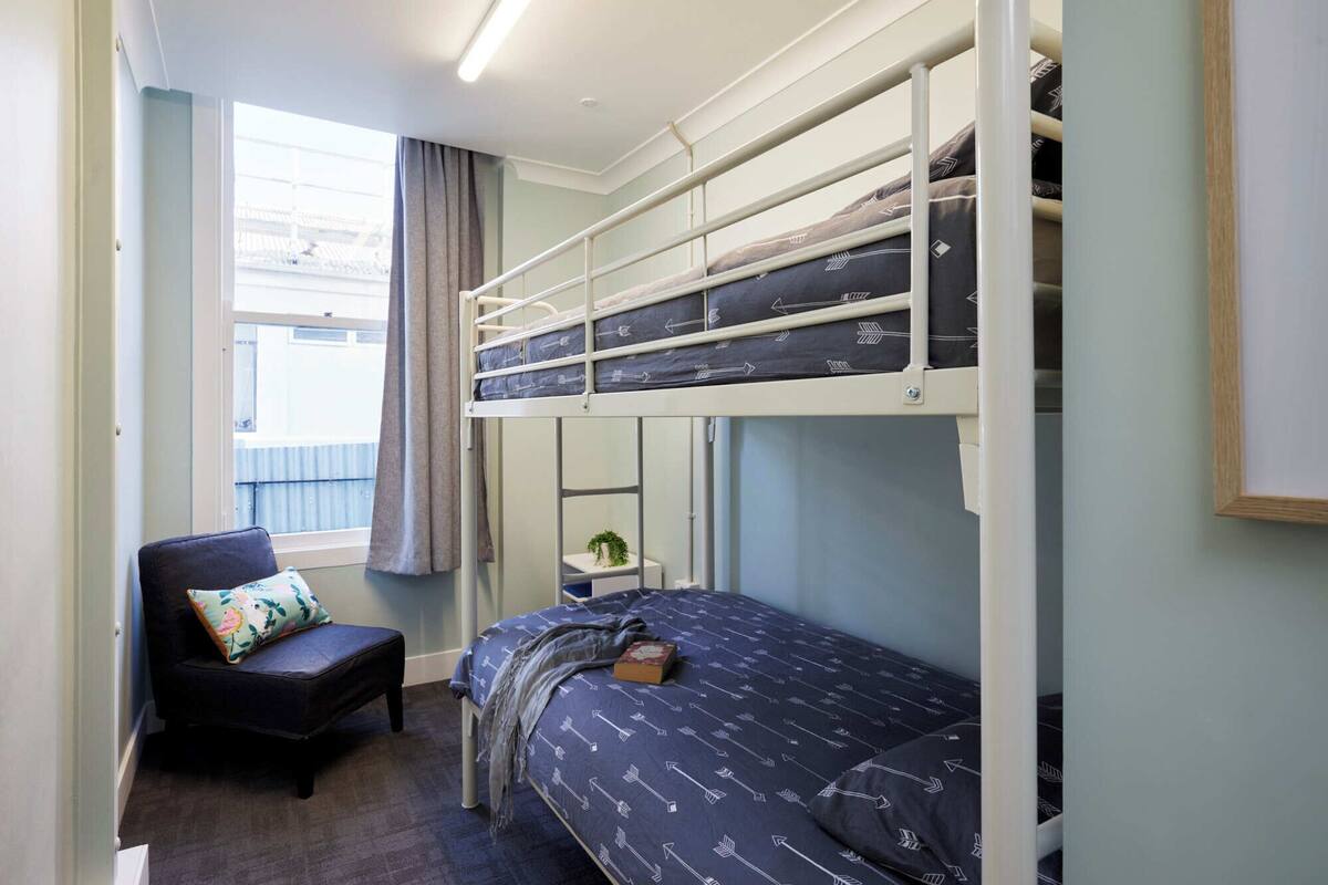 A bunk bed room with a desk and chair, a window with curtains, and a small plant.