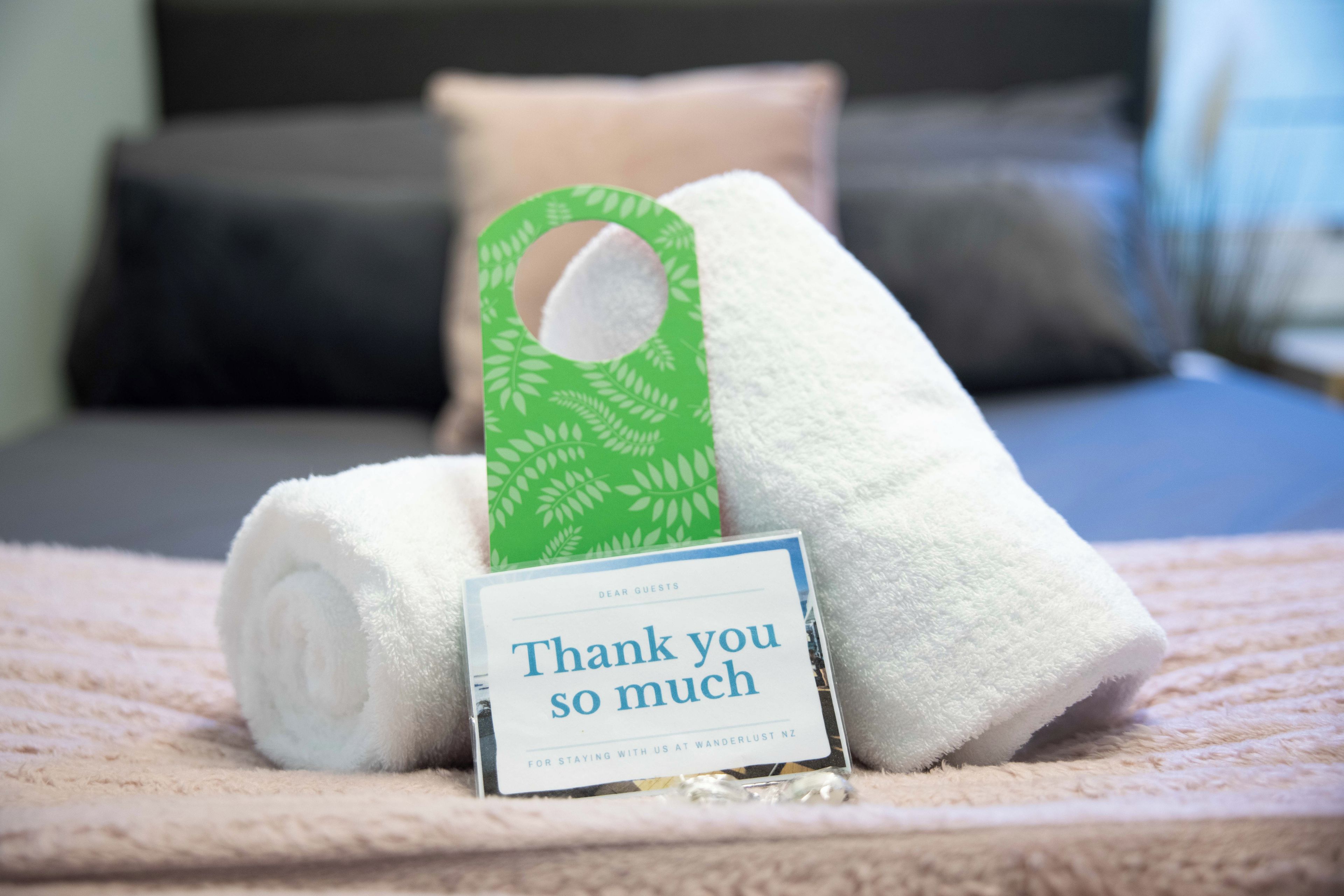 A neatly arranged bed with rolled white towels and a thank you card on a textured bedspread.