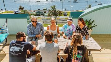 A group of people seated at a wooden table outdoors with a view of boats on the water.